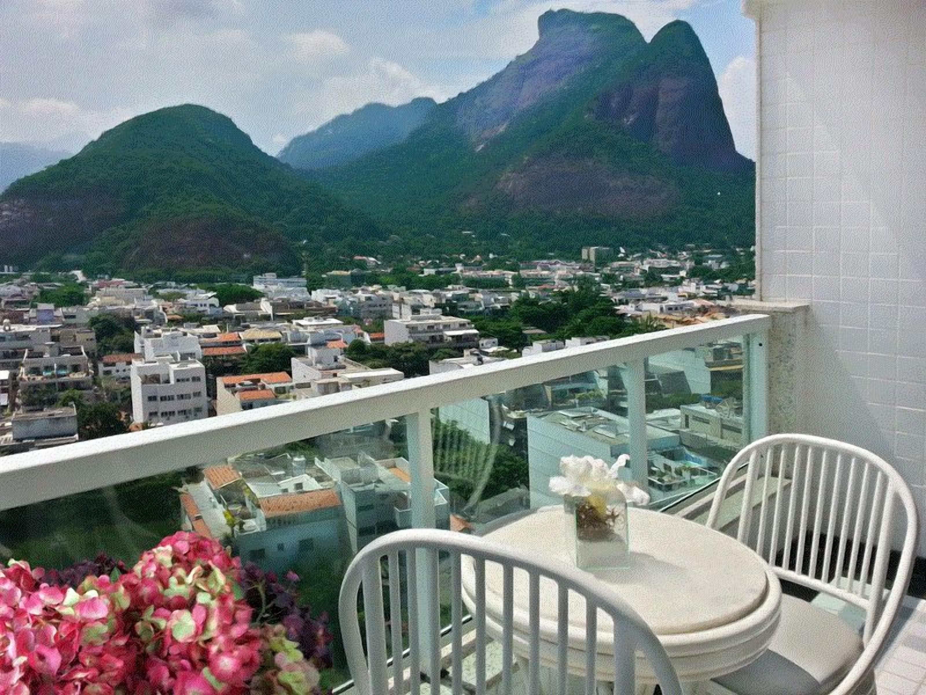 A balcony with a table and chairs, overlooking a cityscape with mountains in the background.
