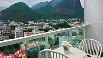 A balcony with a table and chairs, overlooking a cityscape with mountains in the background.