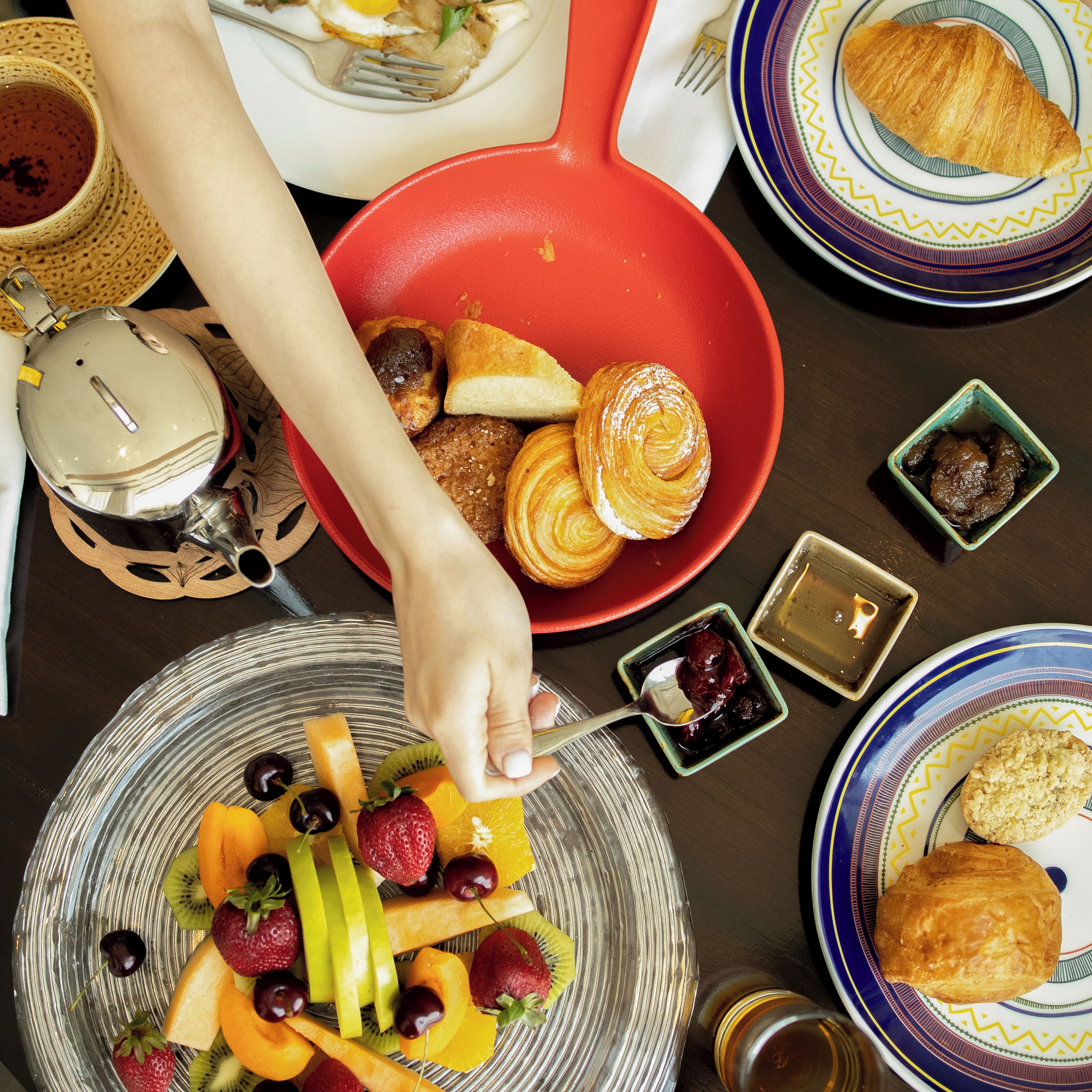 A breakfast setting with a variety of foods including fruits, pastries, and a croissant on a table.