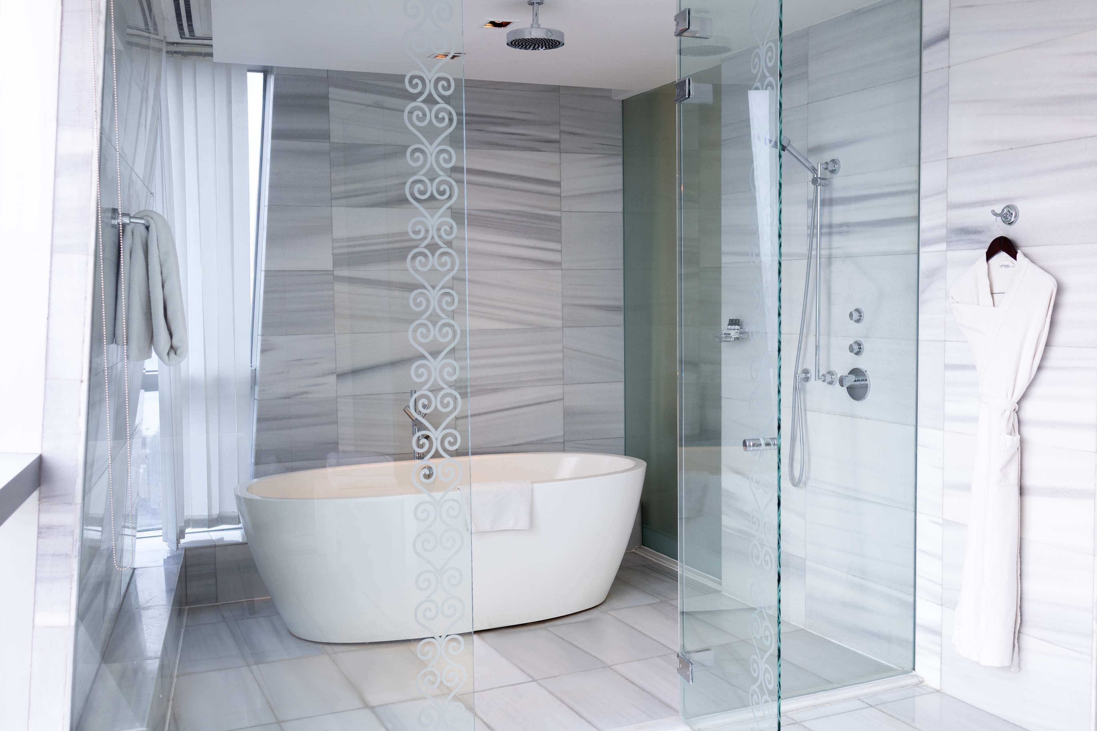 A modern bathroom with a freestanding bathtub, a glass shower enclosure, and a robe hanging on the wall.