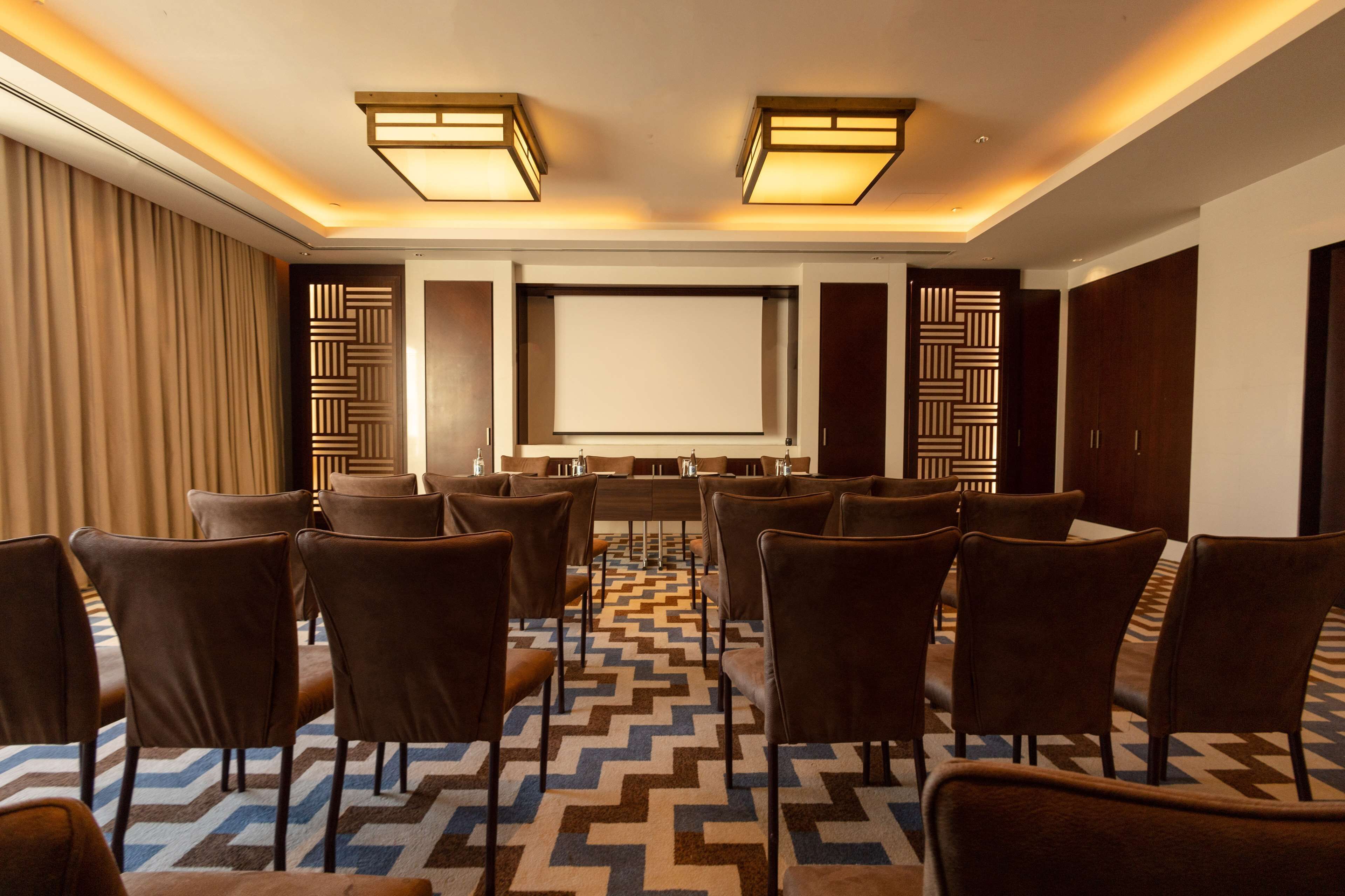 A conference room with a large screen, multiple rows of chairs, and patterned carpet.