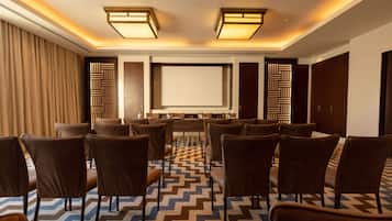 A conference room with a large screen, multiple rows of chairs, and patterned carpet.