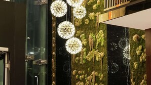 A lobby with a high ceiling, a green wall with spherical decorations, and a seating area with a sofa and armchair.
