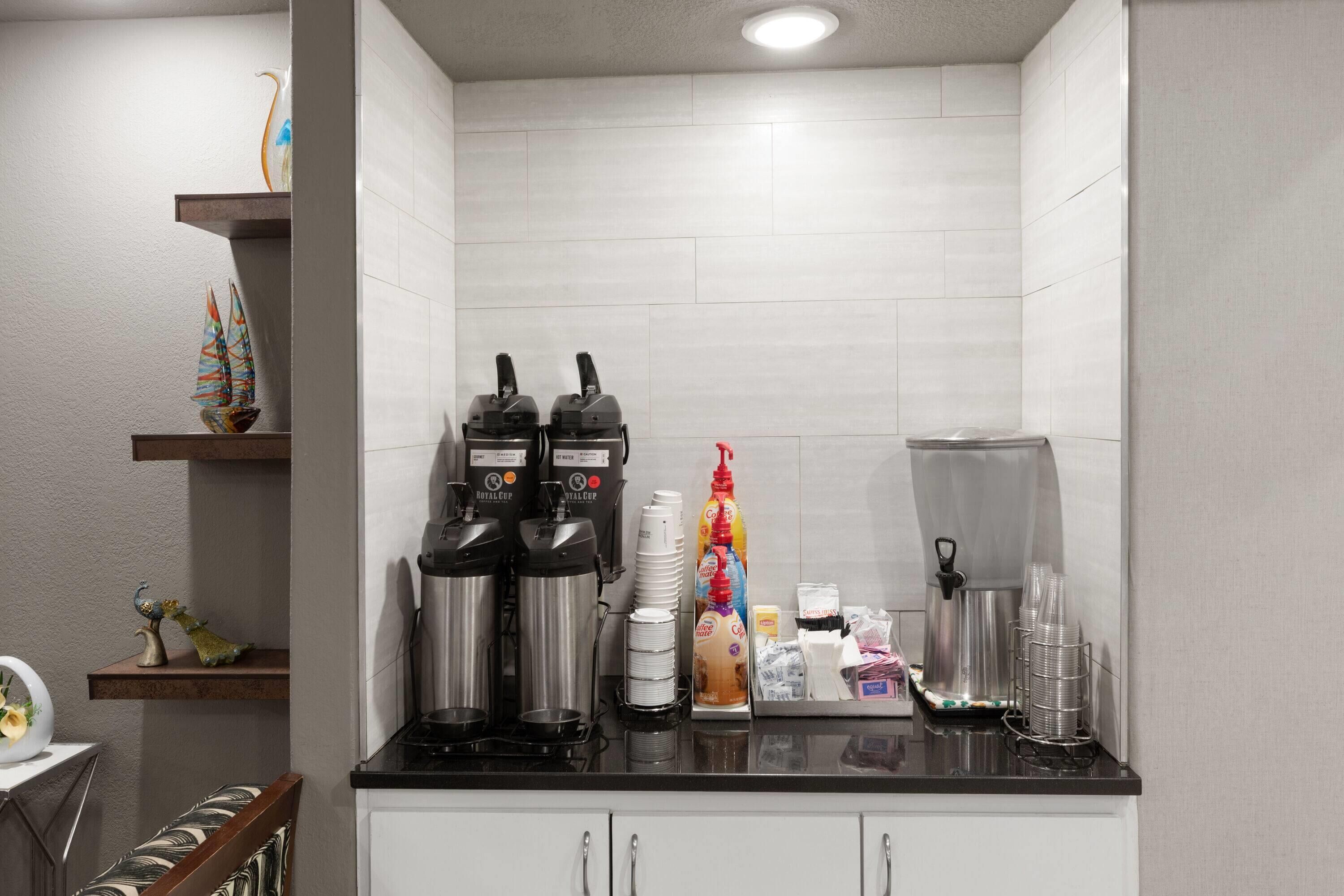 A kitchenette with coffee makers, a coffee dispenser, and a variety of cups and containers.