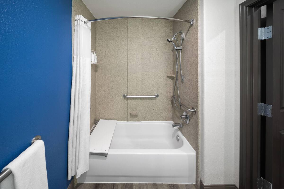 A bathroom with a bathtub, shower, and handrails.