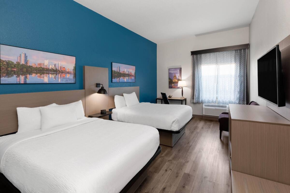 A hotel room with two beds, a desk, a TV, and artwork on the walls.
