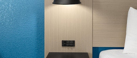 Ein modernes Hotelzimmer mit einem Holzkopfteil, einer schwarzen Wandlampe und einem kleinen Ablageschrank.