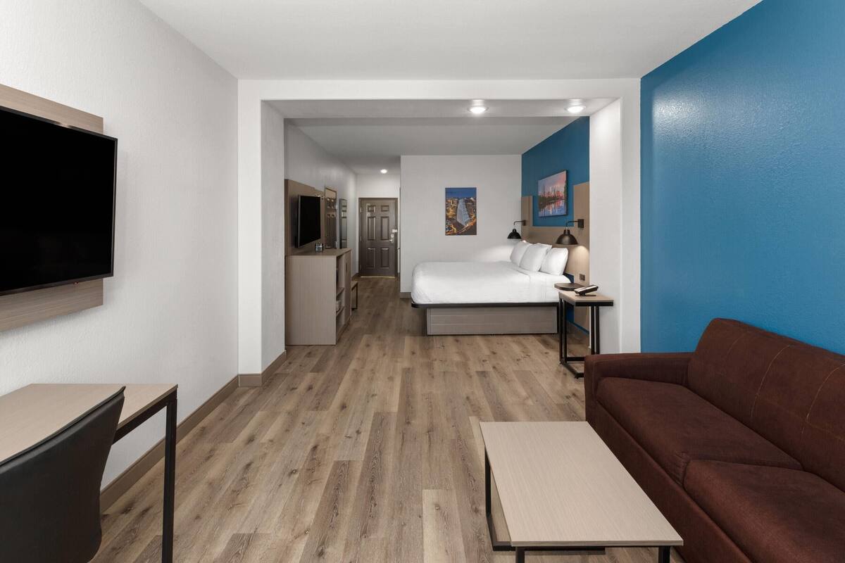 A hotel room with a bed, a brown sofa, a TV, a desk, and a small table.