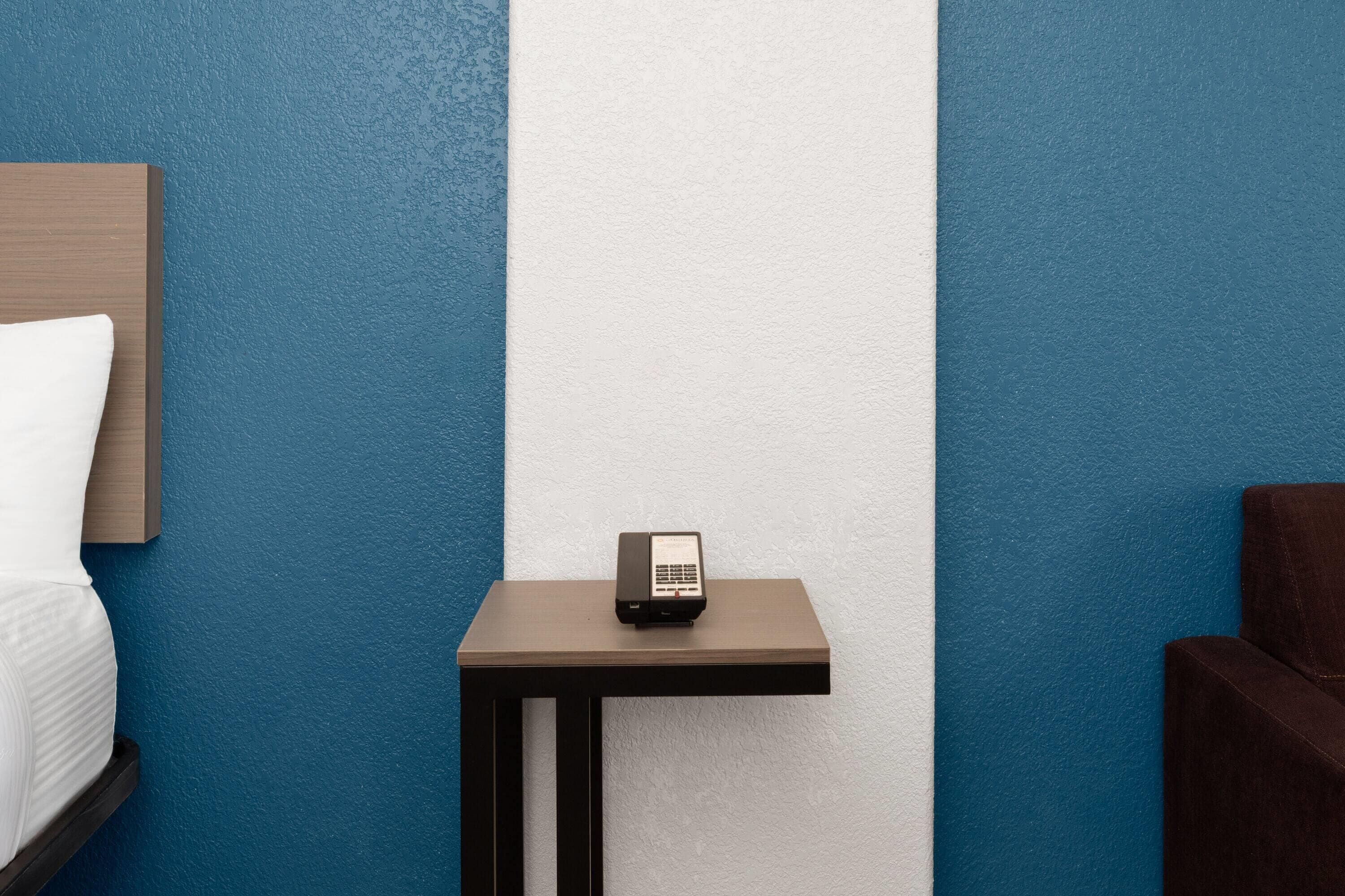 A hotel room with a bed, a small table with a phone, and a brown chair.