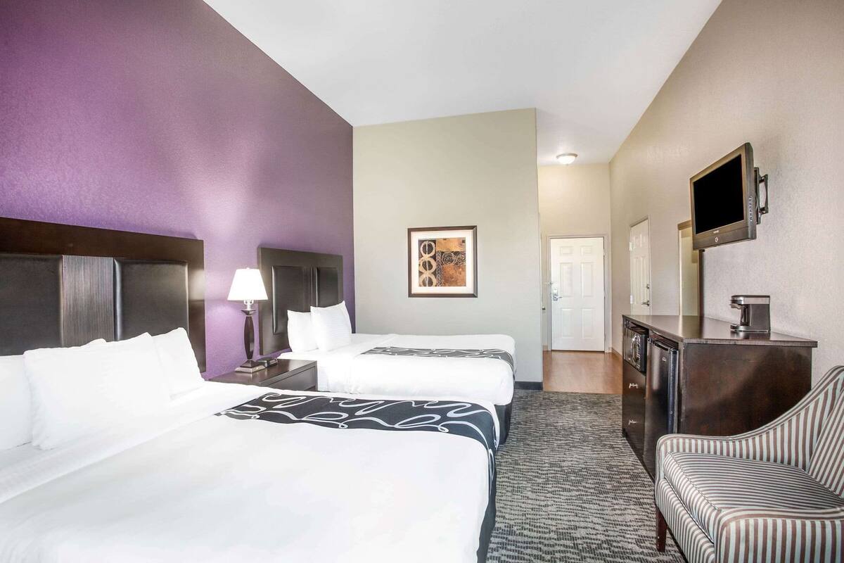 A hotel room with two beds, a desk, a chair, a television, and a framed picture on the wall.