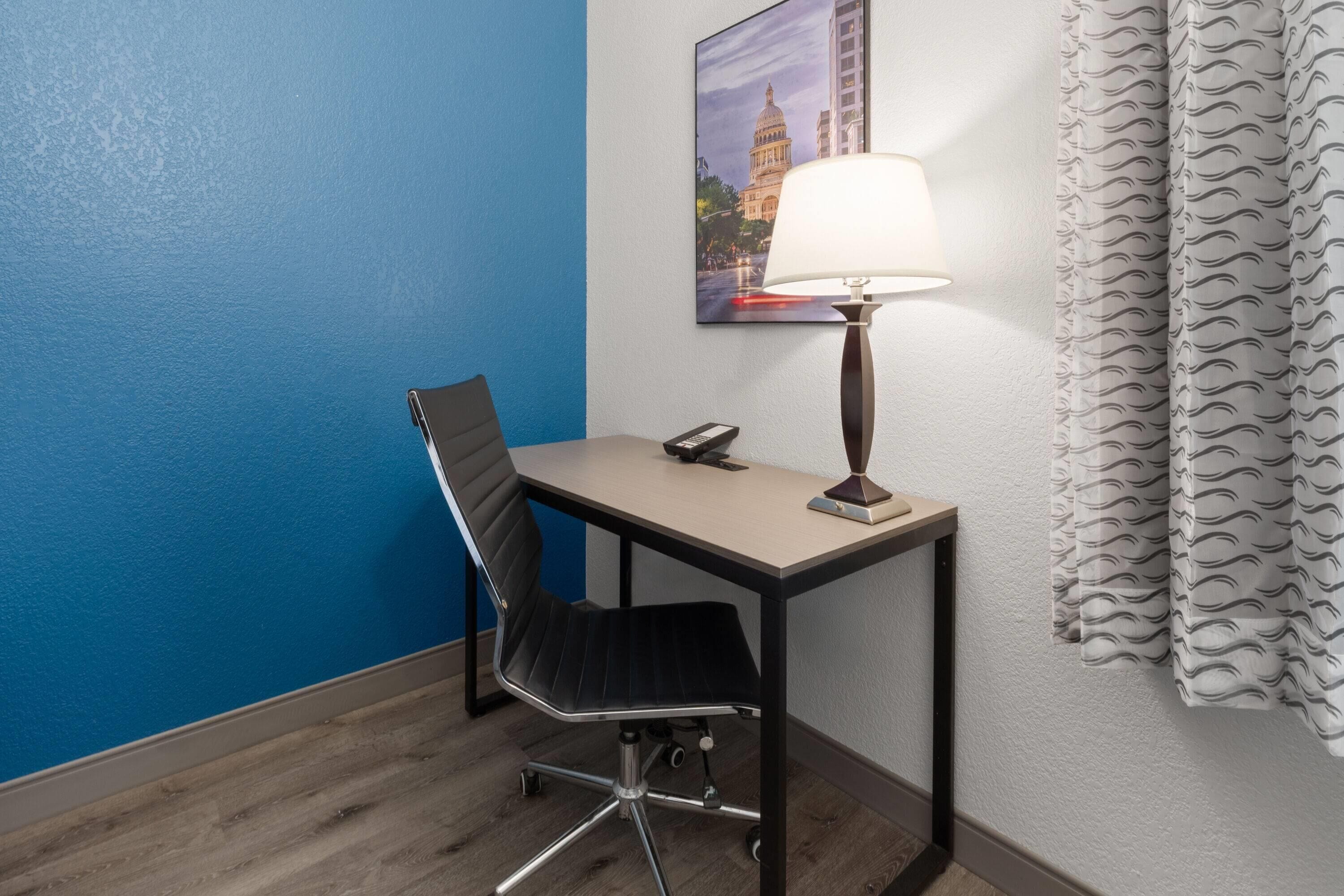 Une chambre d’hôtel équipée d’un bureau, d’une chaise, d’une lampe et ornée d’un tableau représentant un bâtiment.