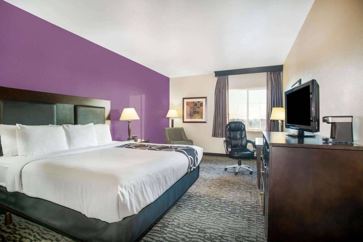 A hotel room with a large bed, two bedside lamps, a desk with a computer, a television, and a coffee maker.