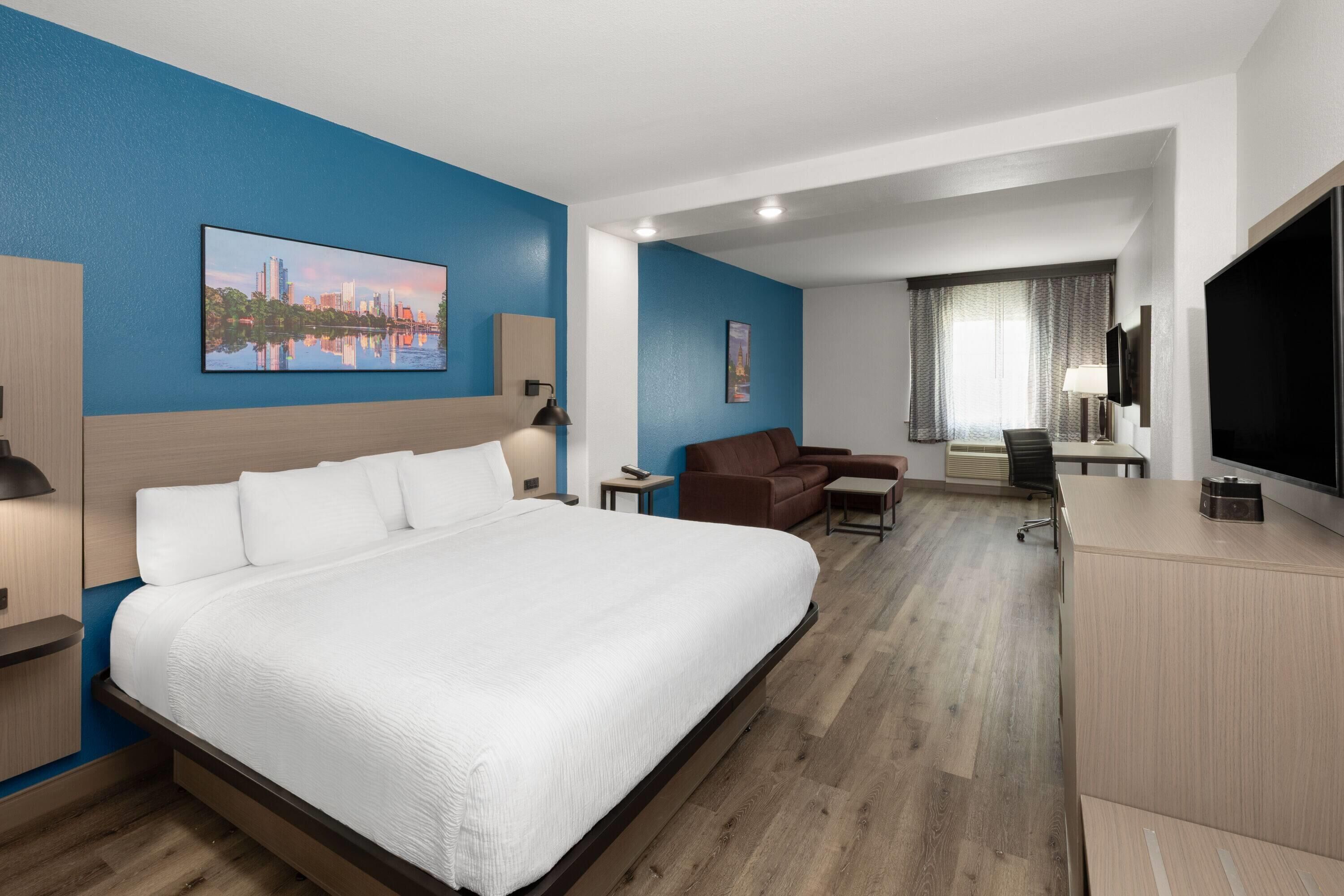 A hotel room with a large bed, a desk, a chair, a TV, and a painting on the wall.