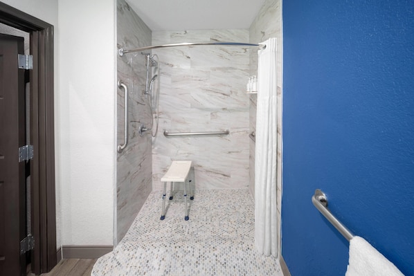 Un baño con ducha, barras de apoyo, un banco blanco y una pared azul.