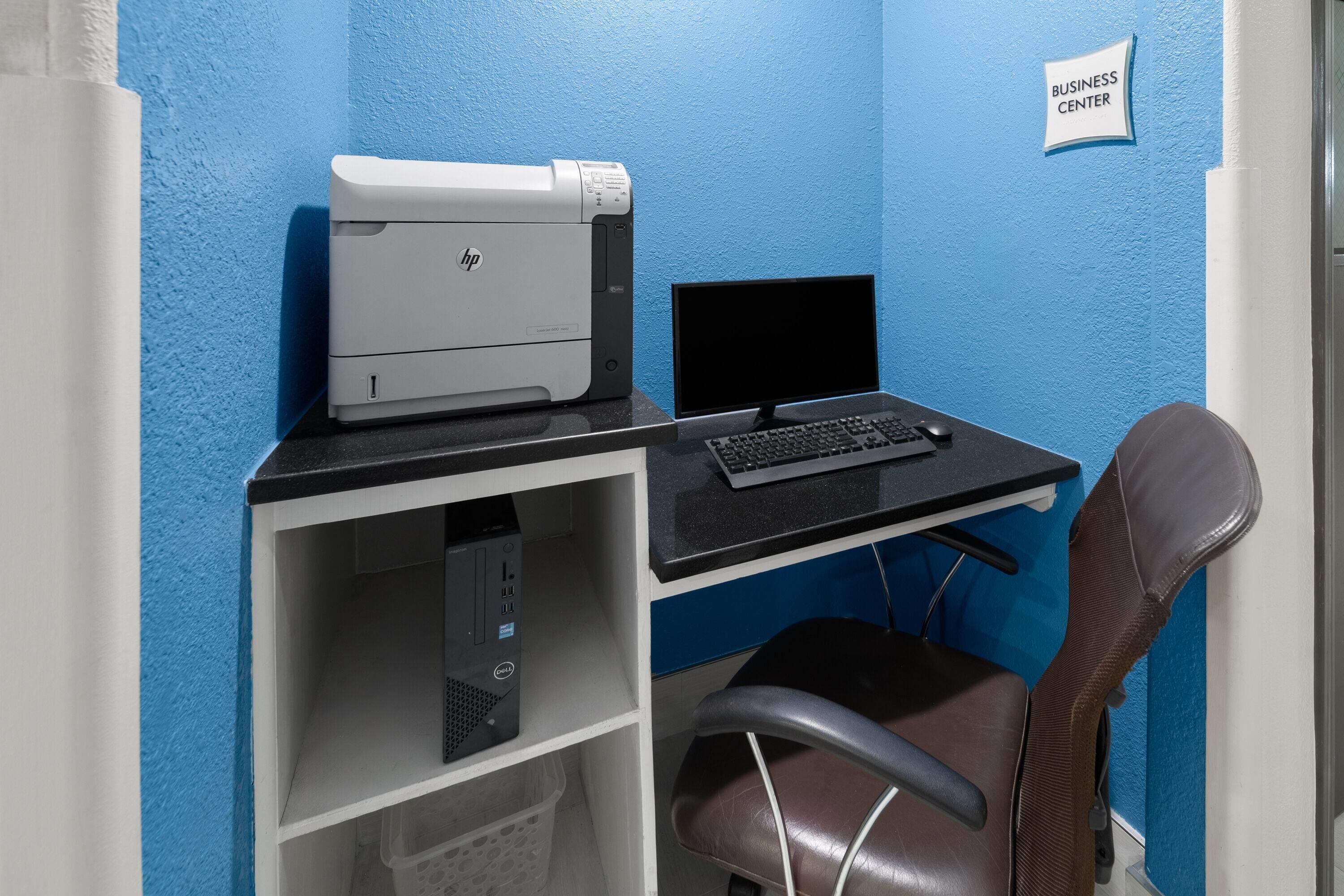 Un espacio de oficina pequeño con una impresora, un monitor, un teclado y una silla.