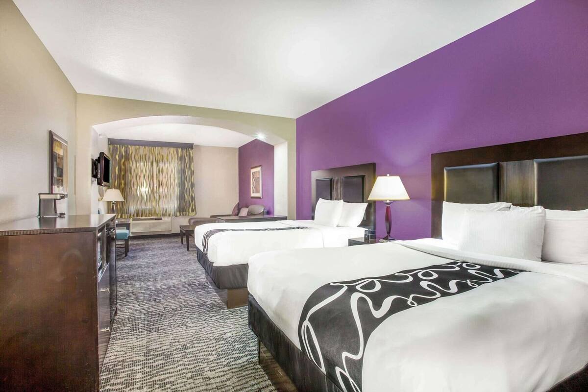 A hotel room with two beds, a desk, a TV, and a bathroom.
