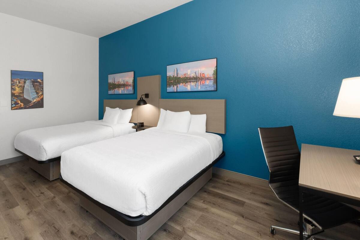 A hotel room with two beds, a desk, and a chair.
