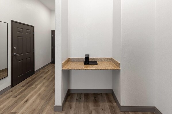 A hallway with a wooden floor, a brown door, and a small countertop with a coffee maker.