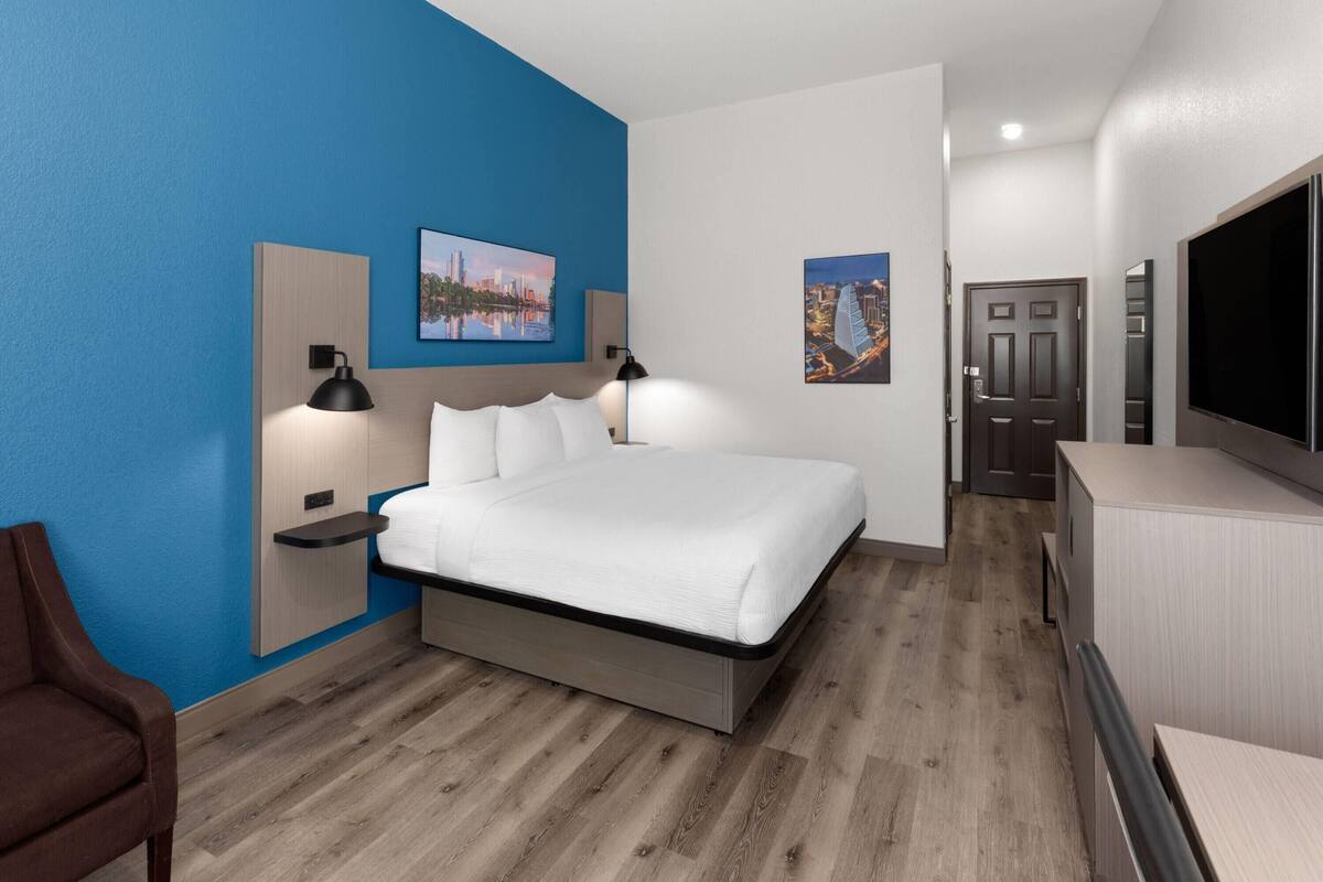 A modern hotel room with a bed, bedside tables, a TV, and artwork on the walls.