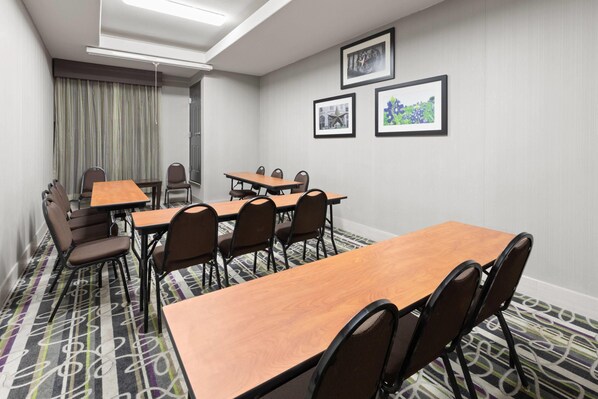 A conference room with a long table, chairs, a projector screen, and framed pictures on the wall.