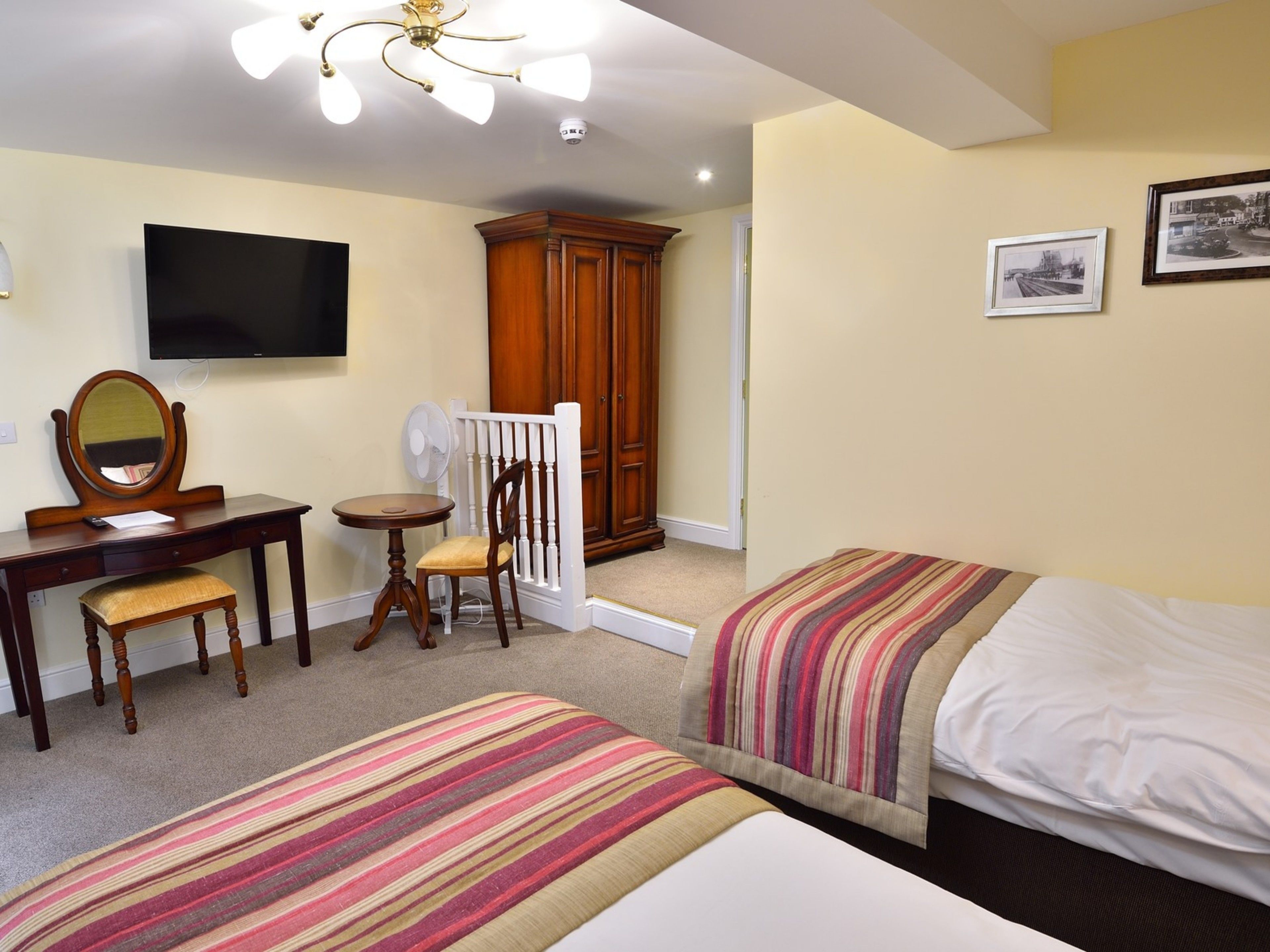 A hotel room with two beds, a desk with a chair, a mirror, a television, and a wardrobe.
