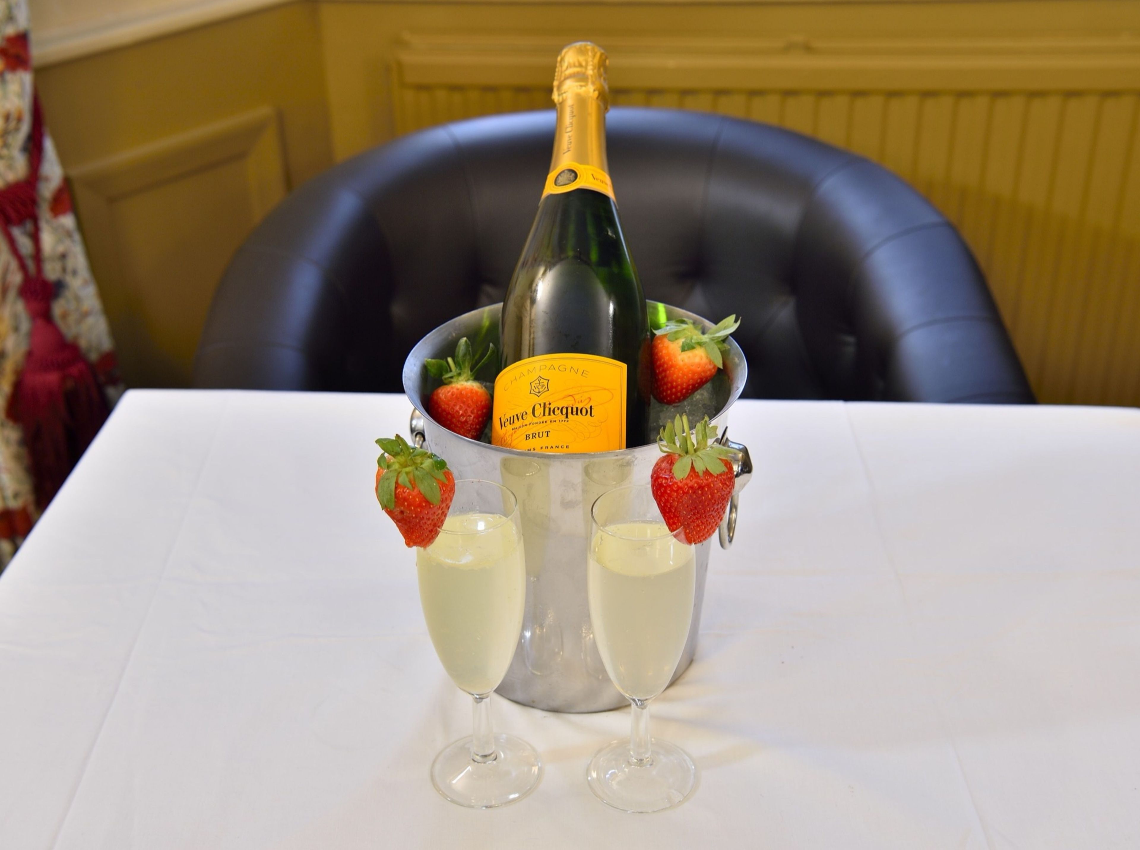 Una botella de champán Veuve Clicquot en un cubo plateado, junto con dos copas de champán y fresas.