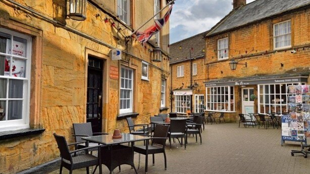 A traditional pub with outdoor seating, a flag, and a sign indicating a restaurant. - The George Hotel, Crewkerne (Crewkerne)
