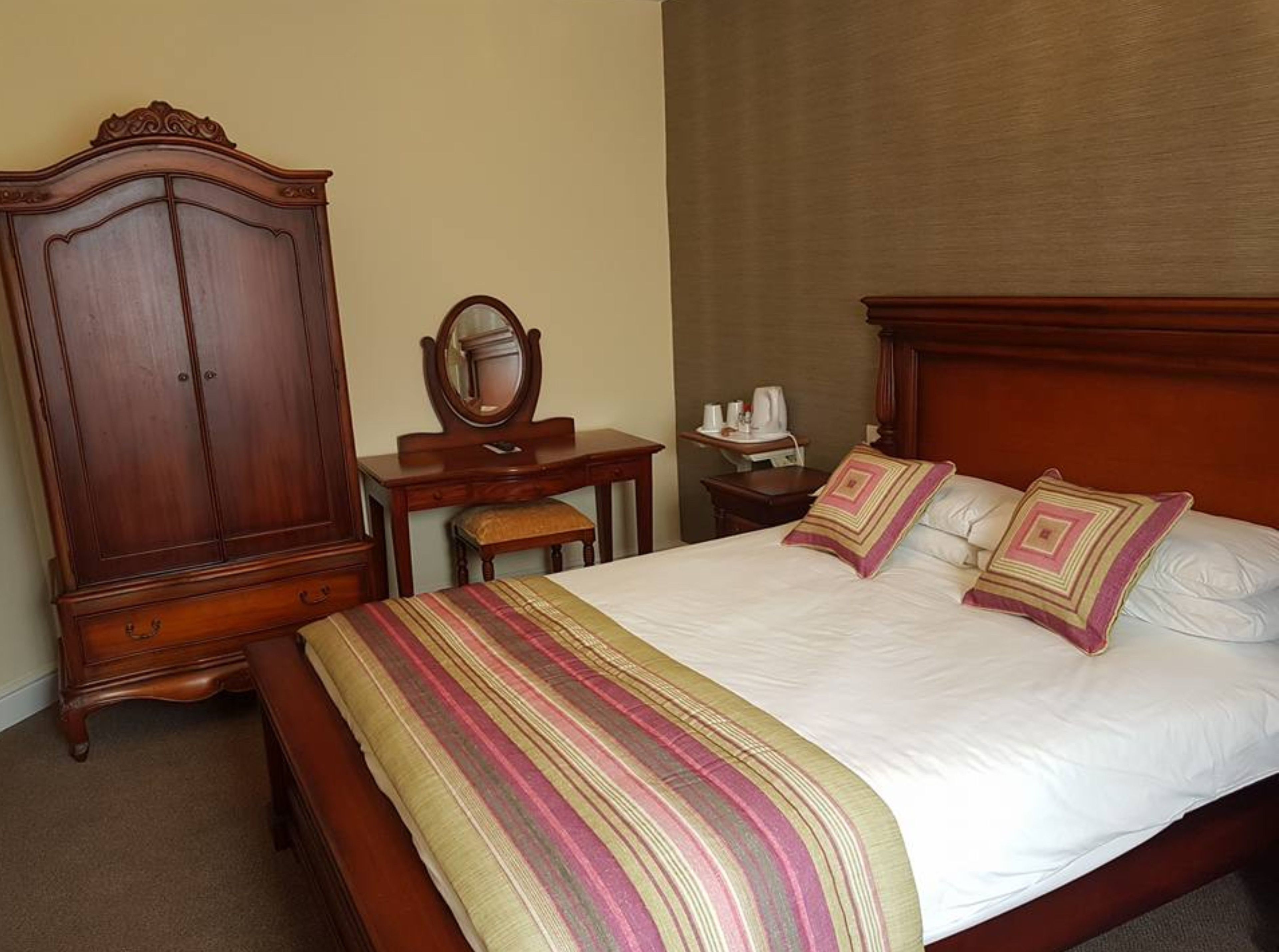 Un dormitorio con una cama grande de madera, un aparador de madera, una mesita de noche con un espejo y un escritorio pequeño con una silla.
