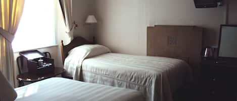 Habitación de hotel con dos camas individuales, un escritorio, un teléfono, una lámpara y televisión en la pared.