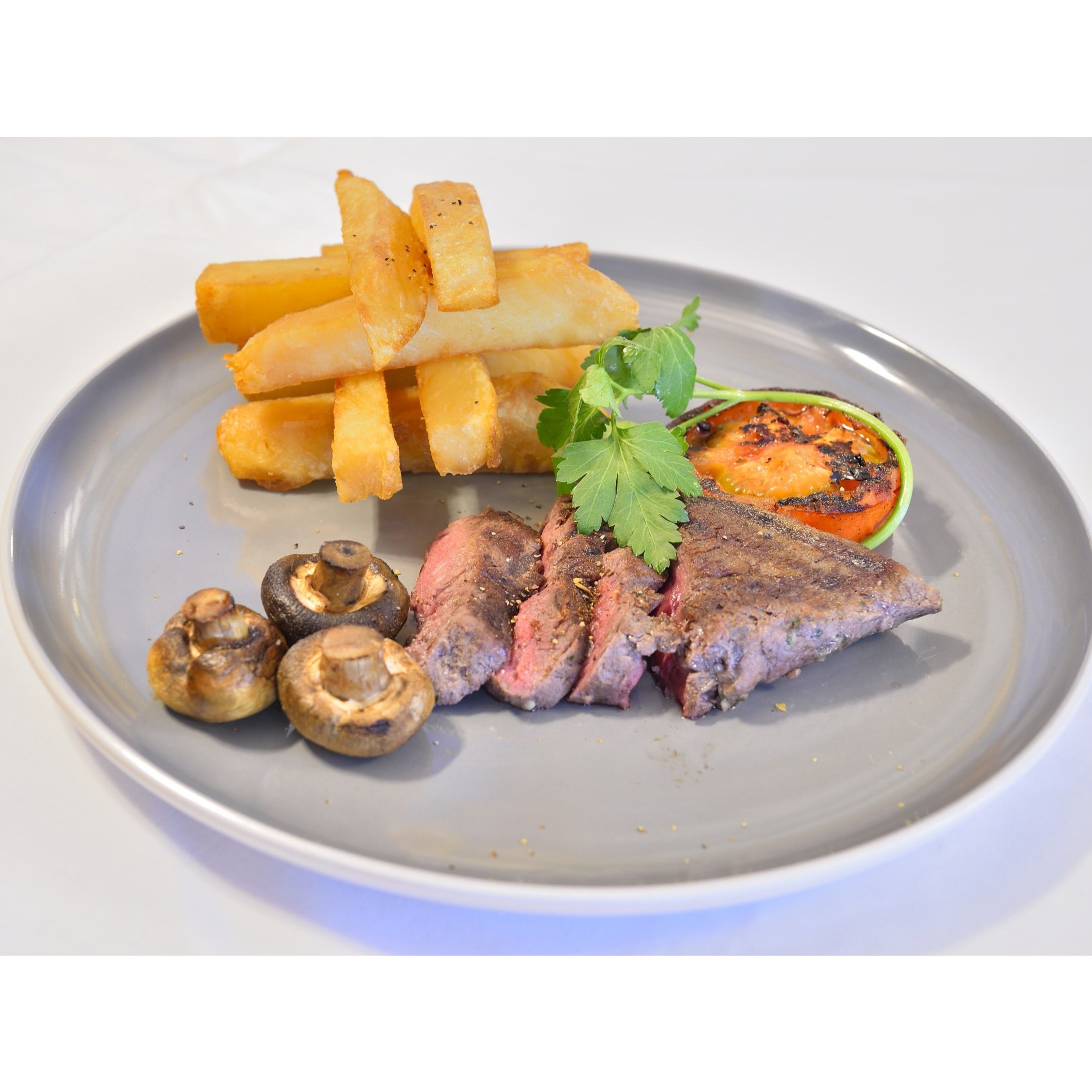 A plate with steak, mushrooms, fries, and a grilled tomato.
