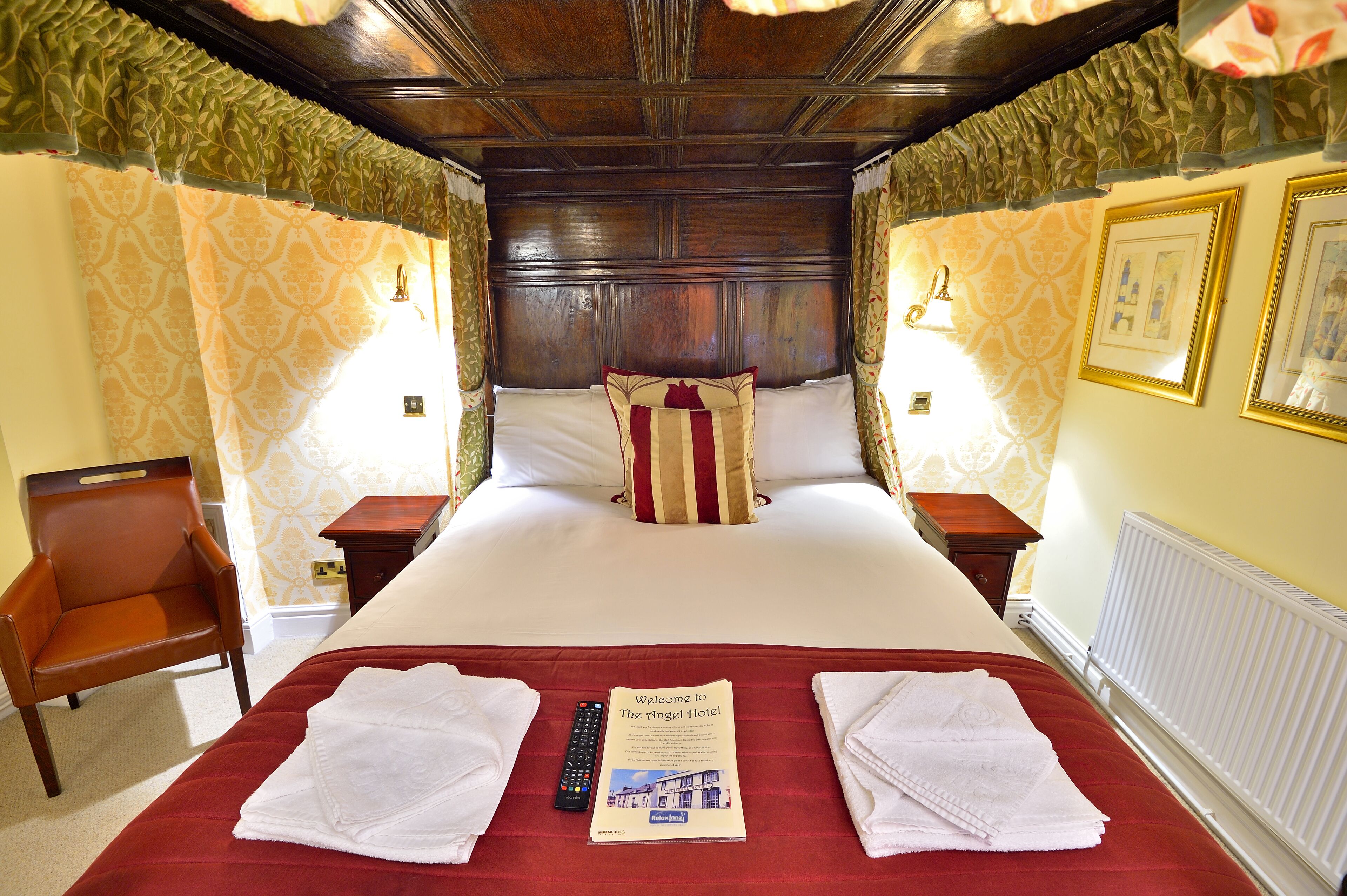 A hotel room with a large bed, a wooden headboard, two nightstands, a chair, and a welcome brochure.