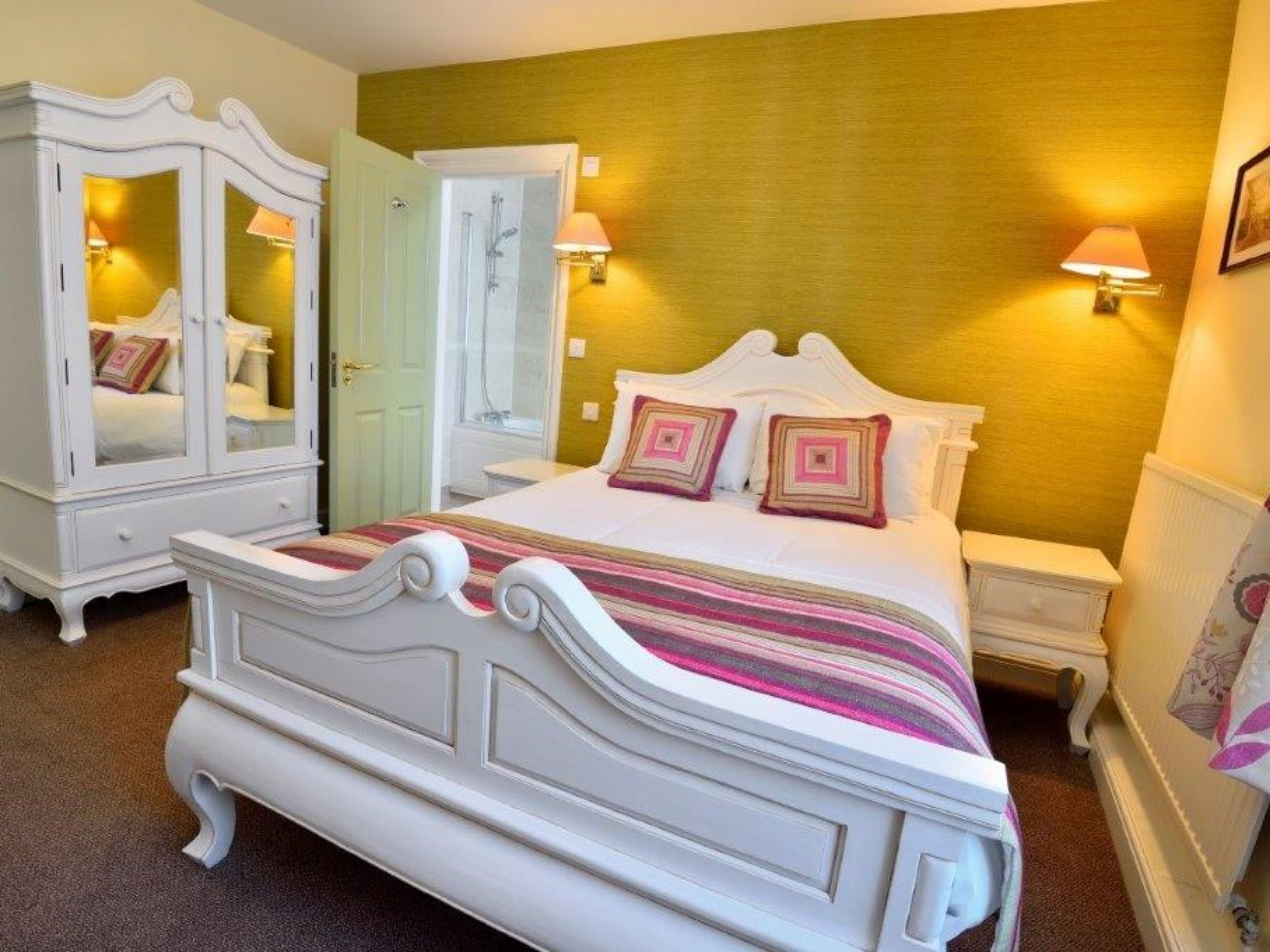 A bedroom with a large bed, a wardrobe, a mirror, and two bedside lamps.