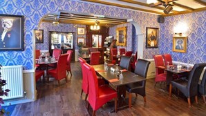 A restaurant with red and black upholstered chairs, wooden tables, and patterned wallpaper. - The George Hotel, Crewkerne (Crewkerne)
