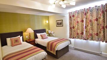 A hotel room with two beds, a ceiling fan, a window with floral curtains, and a framed picture on the wall.