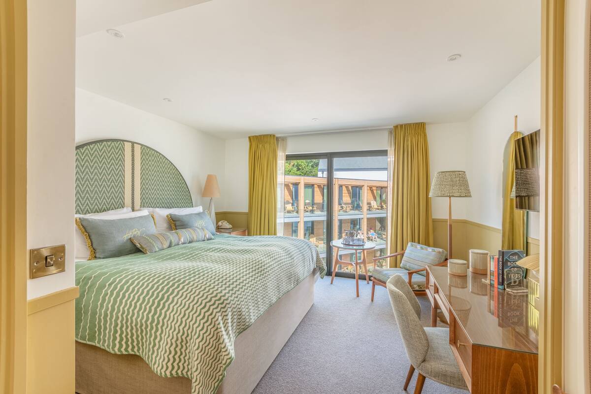 A hotel room with a large bed, a desk with a chair, a small table, and a view of the outside.