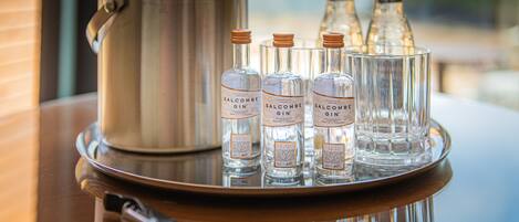 A tray with three bottles of Salcombe Gin and a metal pot on a reflective surface.