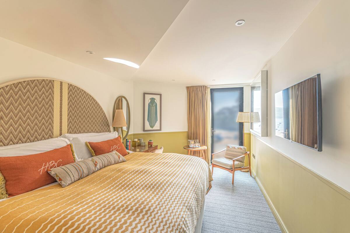 A hotel room with a large bed, a small table, a chair, a TV, and a window with curtains.