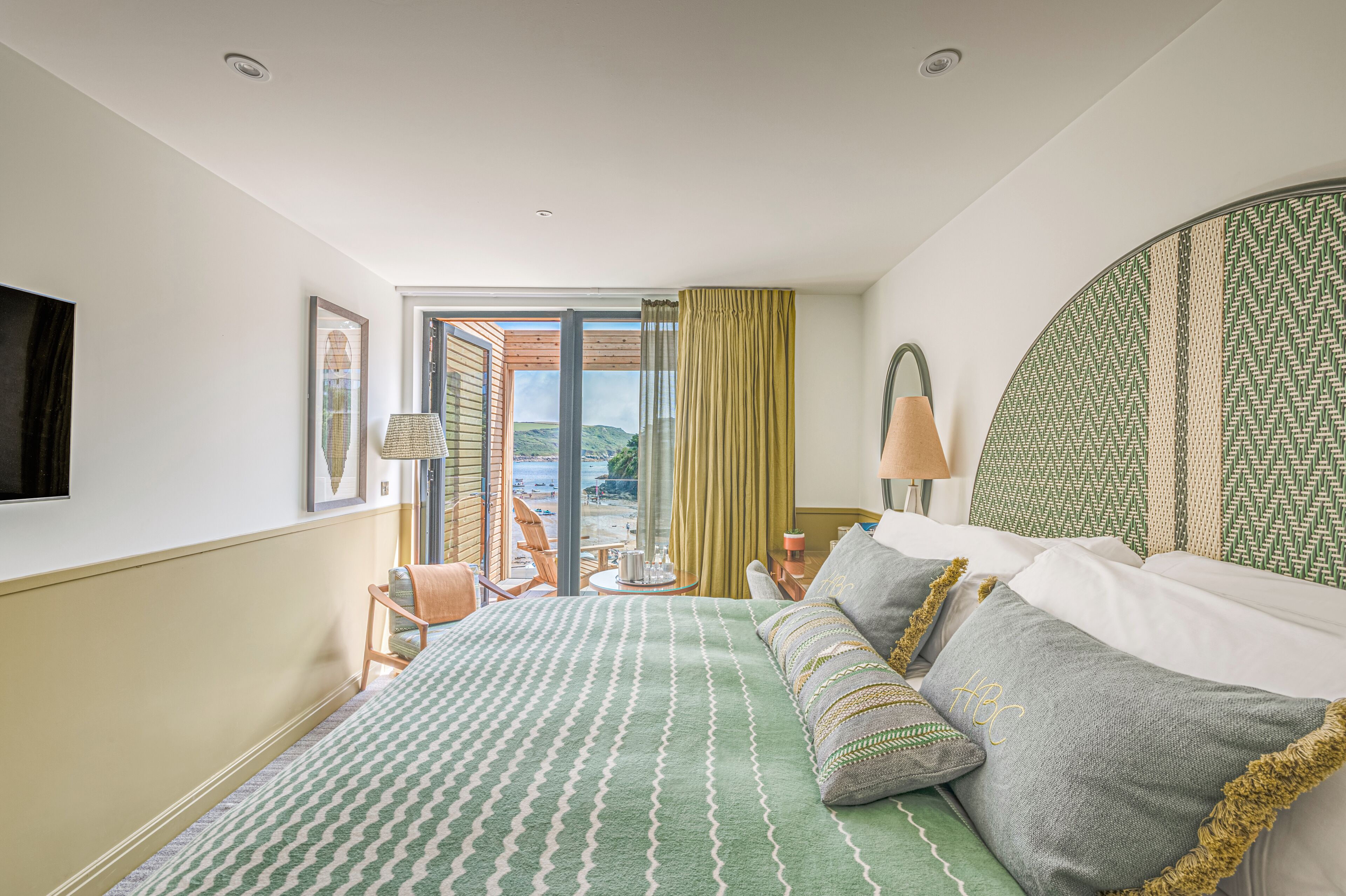 Habitación de hotel con una cama grande, vista al mar, ventana con cortinas y televisor montado.