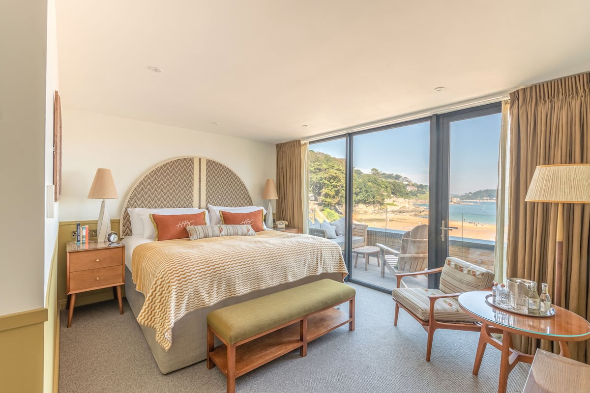 A hotel room with a bed, a bench, a table with drinks, and a view of the beach.
