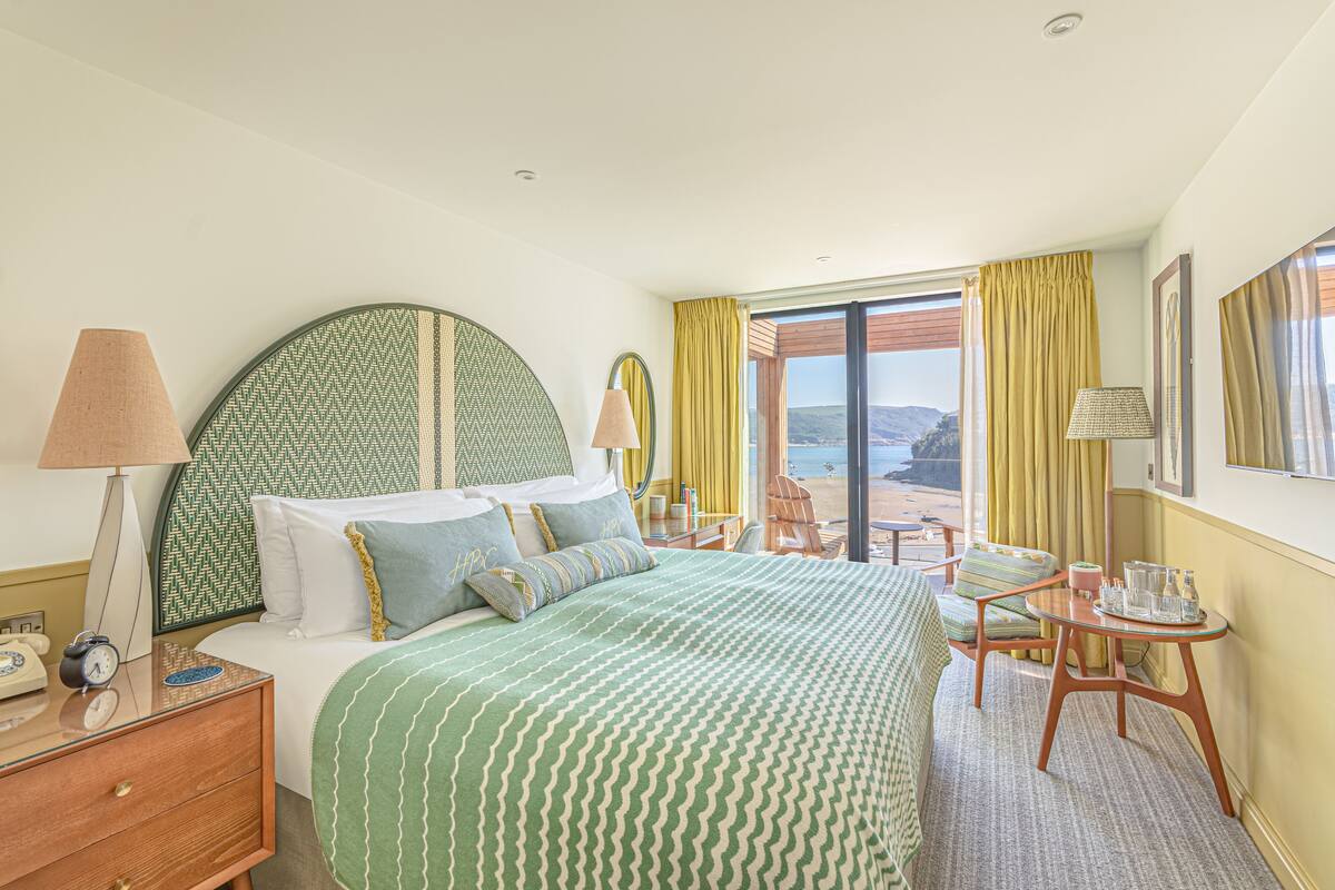 A hotel room with a large bed, a desk, a chair, and a view of the beach.