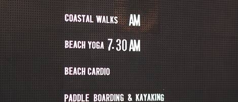 Pantalla digital que muestra las actividades del resort, entre ellas: servicio de transporte, ferry, helados, paseos costeros, yoga en la playa, ejercicios cardiovasculares en la playa y remo y kayak.