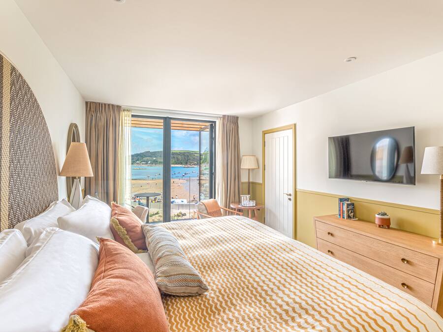 A hotel room with a large bed, a TV, a dresser, and a view of the beach.