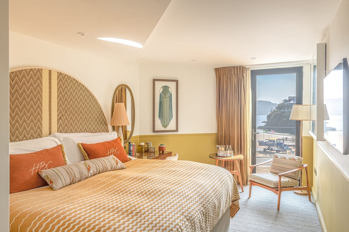 A hotel room with a large bed, a chair, a table, and a view of the beach.