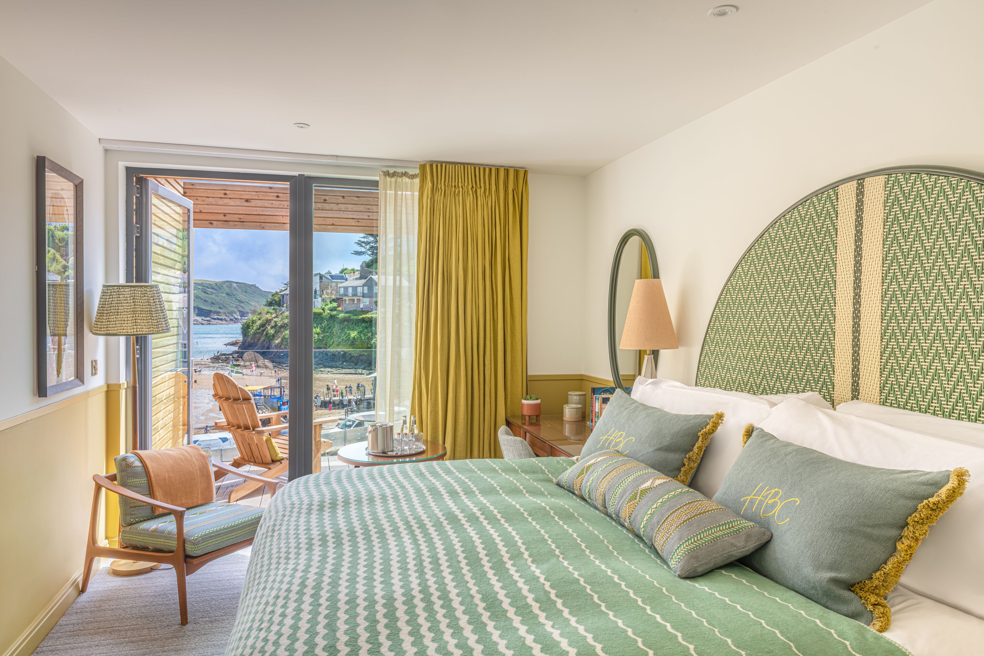 A hotel room with a large bed, a view of the beach, and a balcony with outdoor seating.