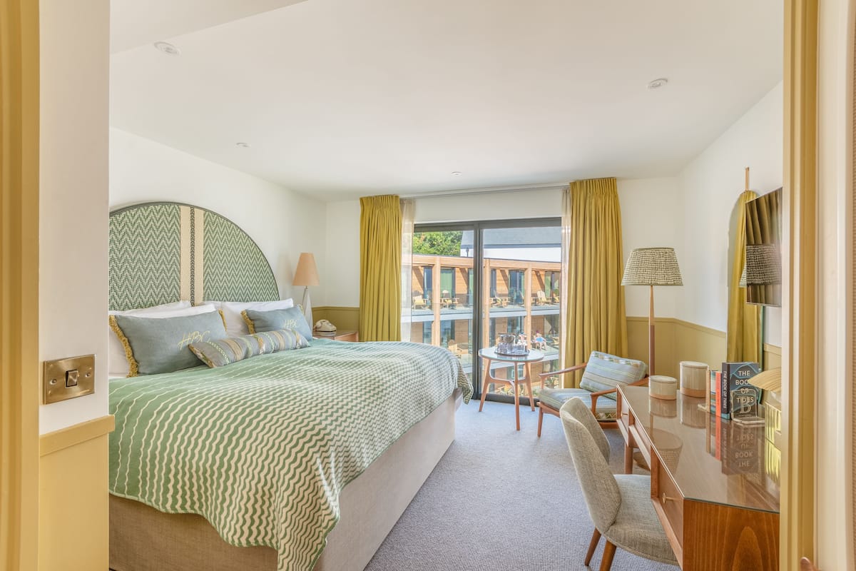 A hotel room with a large bed, a desk, a chair, a table, and a balcony with a view.