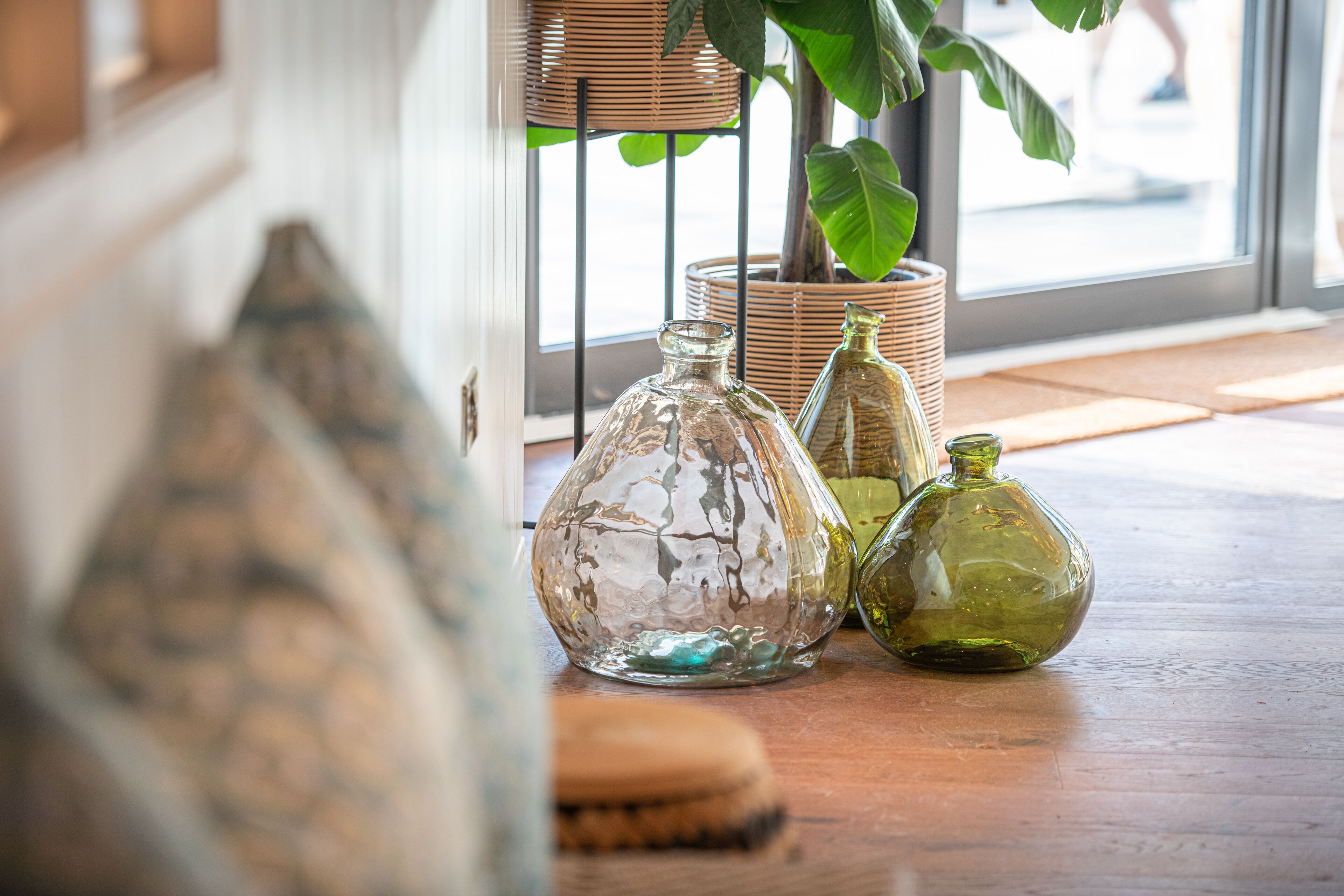 A wooden table with three glass bottles and a woven basket with a plant.