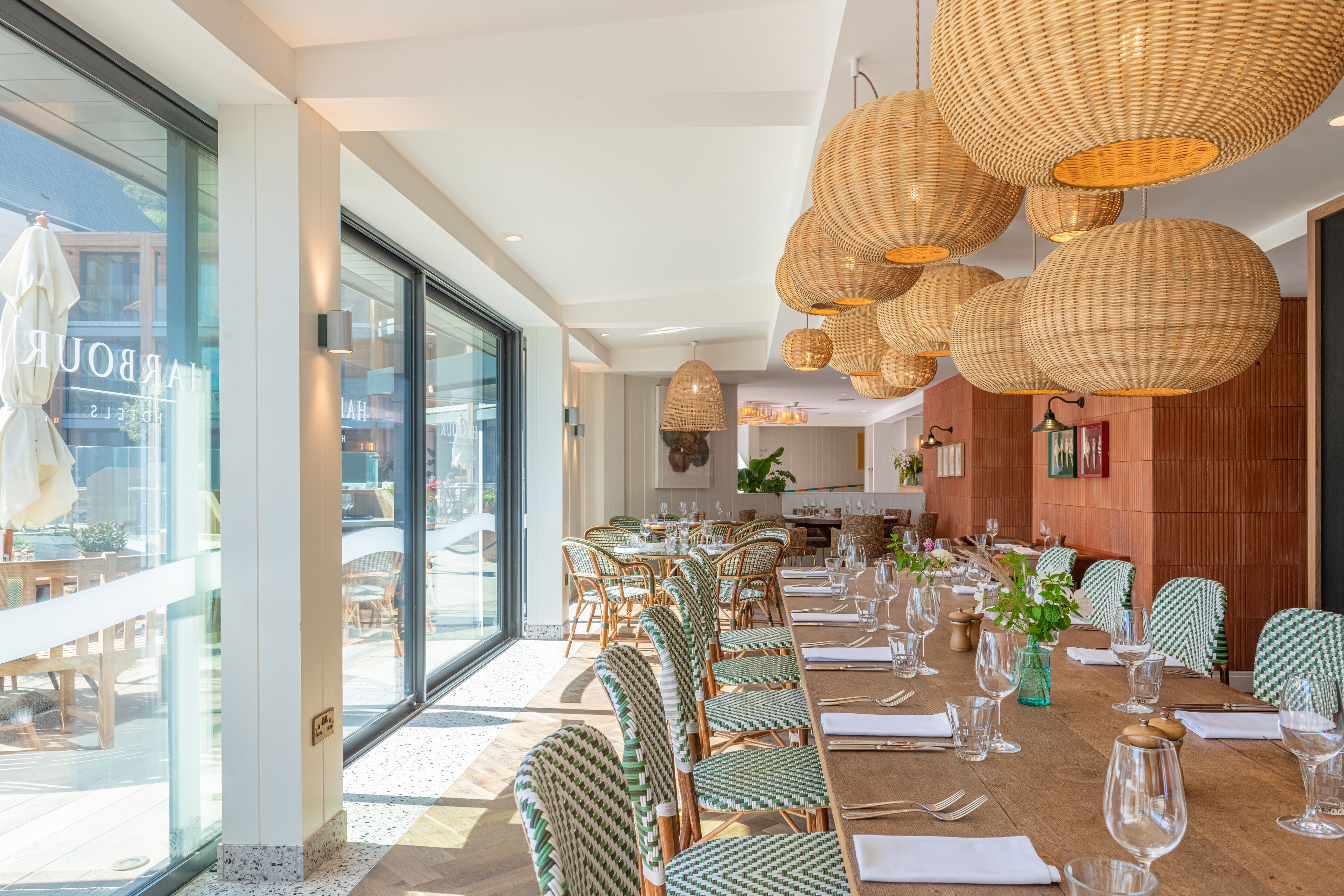 Un comedor con lámparas colgantes de mimbre, sillas de madera y una larga mesa preparada para una comida.