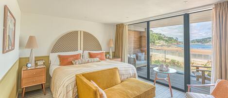 A hotel room with a bed, a sofa, a small table, and a view of the beach.