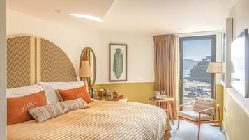 A hotel room with a large bed, a view of the beach, and a small table with a lamp.