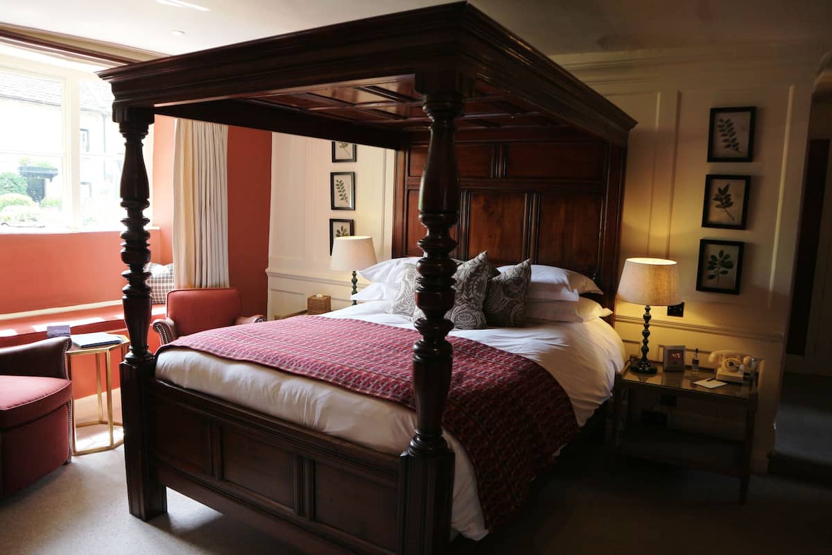 Uma cama com dossel e mosquiteiro vermelho, uma mesa de cabeceira com abajur e quadros nas paredes.